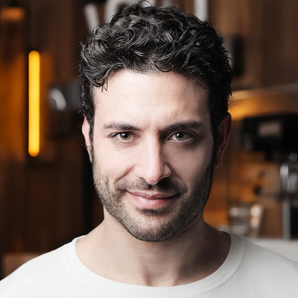 Smirking man with dark hair and five o'clock shadow