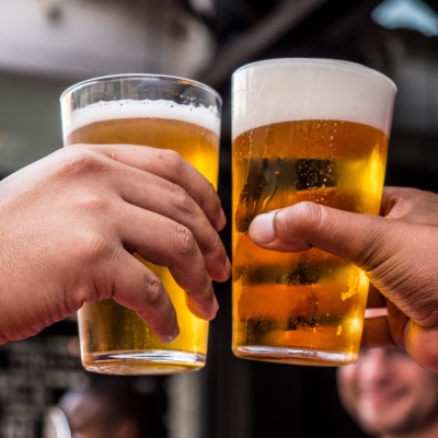 Two hands clinking pint glasses of beer