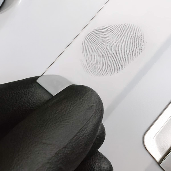 Gloved hand holding strip of paper with a fingerprint on it