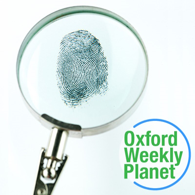 Magnifying glass focused on a fingerprint with the Oxford Weekly Planet logo in the foreground
