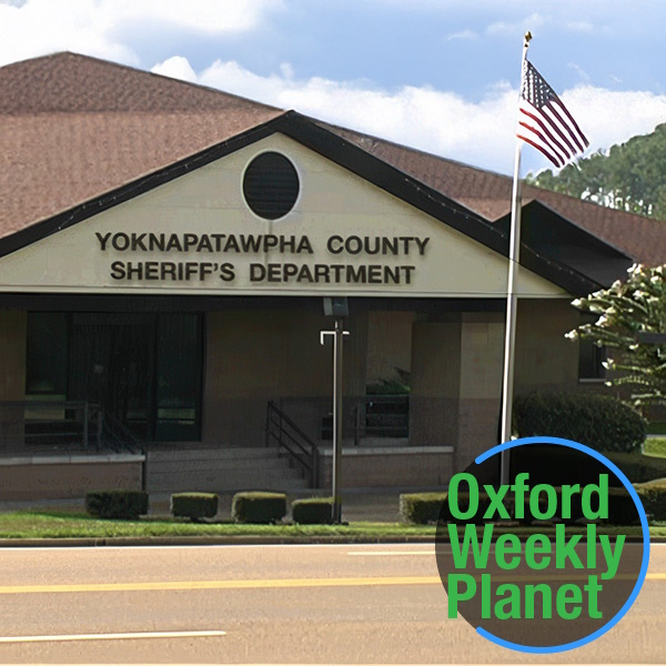 Exterior of the Yoknapatawpha County Sheriff's Department with the Oxford Weekly Planet logo in the foreground