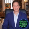 Serious man with short brown hair in a library with the Oxford Weekly Planet logo in the foreground