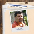 Photo of a man with short dark hair and facial hair clipped to a manila folder