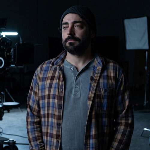 Man with dark hair and beard standing on an empty movie set