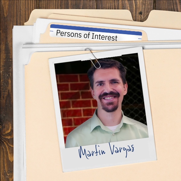 Manila folder with a photo of a smiling man with short dark hair, mustache and goatee clipped to it