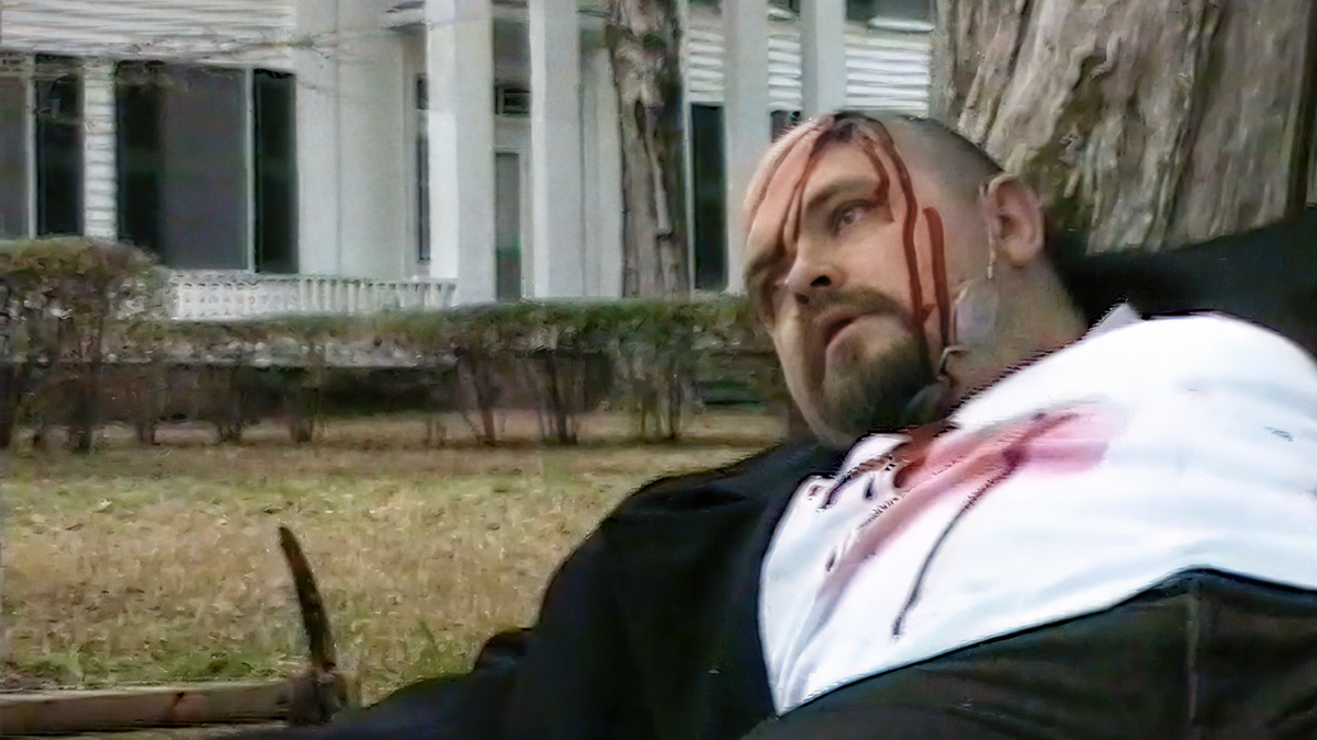 A man on the ground with a head wound. A pick axe is nearby and a southern mansion in the background, home of William Faulkner