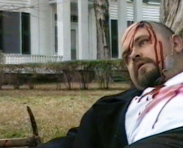 A man on the ground with a head wound. A pick axe is nearby and a southern mansion in the background, home of William Faulkner