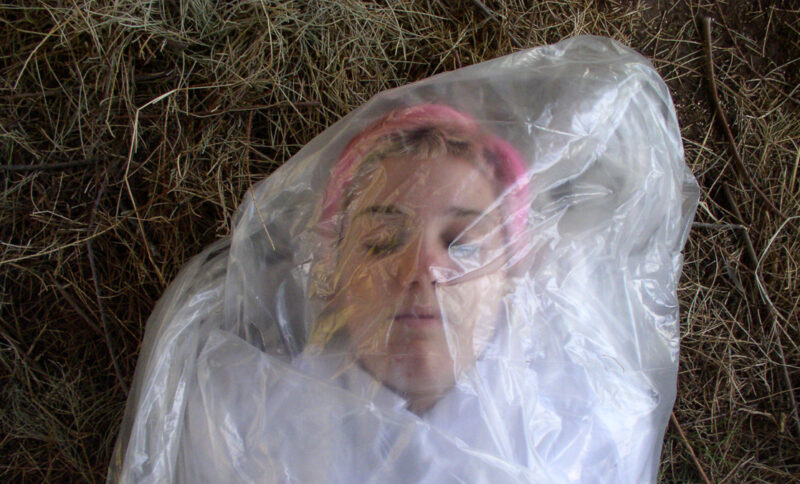 A woman wrapped in plastic and seems to be dead. Her eyes are closed