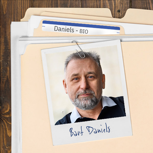 We see a file folder on a desk. Clipped to the folder is a picture of a man with salt and pepper hair and goatee
