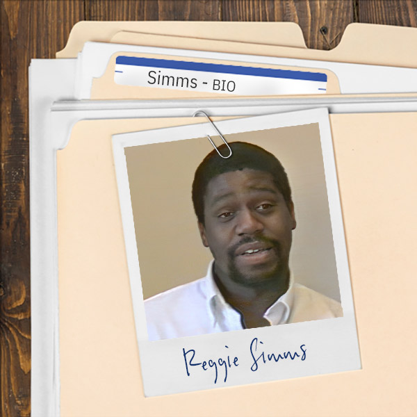 We see a file folder on a desk. Clipped to the folder is a picture of a man with dark hair, mustache, and goatee