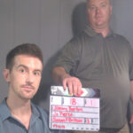 a picture of 2 men, one holding up a clapperboard.