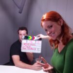a ginger lady holding up a clapboard Infront of a man