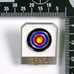 A picture of a bullseye target pin taken near a 90-degree measuring ruler.