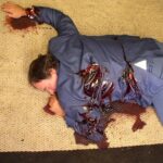 Picture of a man in a blue suit with blood and stab marks on his back