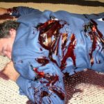 Picture of a man in a blue suit with blood and stab marks on his back
