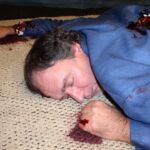 closeup of a dead body with blood pooling from underneath the hand.