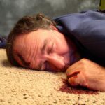 near floor view of a dead body with blood pooling from underneath the hand.