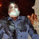 An overhead picture of a pale body with blood pooling around him.