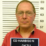 A picture of a mugshot taken of a man in a red polo shirt with a card.
