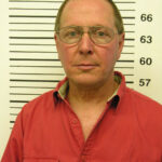 A picture of a mugshot taken of a man in a red polo shirt without a card.