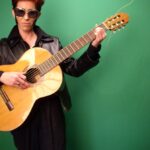 A picture of a person standing infront of a green screen with a guitar