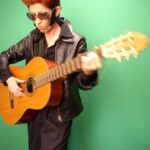 A picture of a person standing infront of a green screen with a guitar