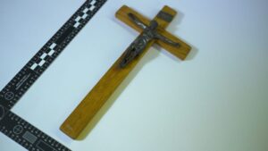 Wooden cross with metal Jesus figurine against the cross. Black "L" shaped forensic ruler surrounding the left and bottom side of the cross.