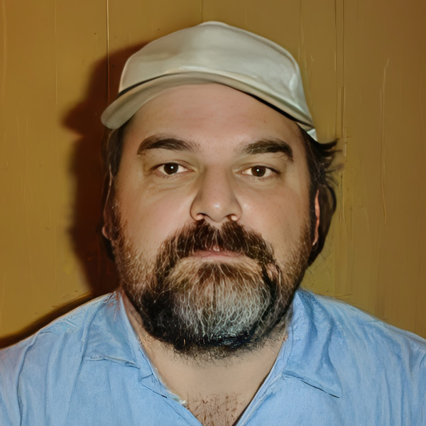 Dark-haired man with a round face and dark facial hair, wearing a baseball cap