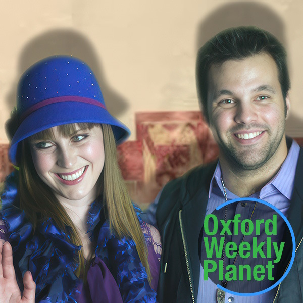 Smiling brunette woman in a blue hat, waving, alongside a smiling man with dark hair and scruffy facial hair with the Oxford Weekly Planet logo in the foreground